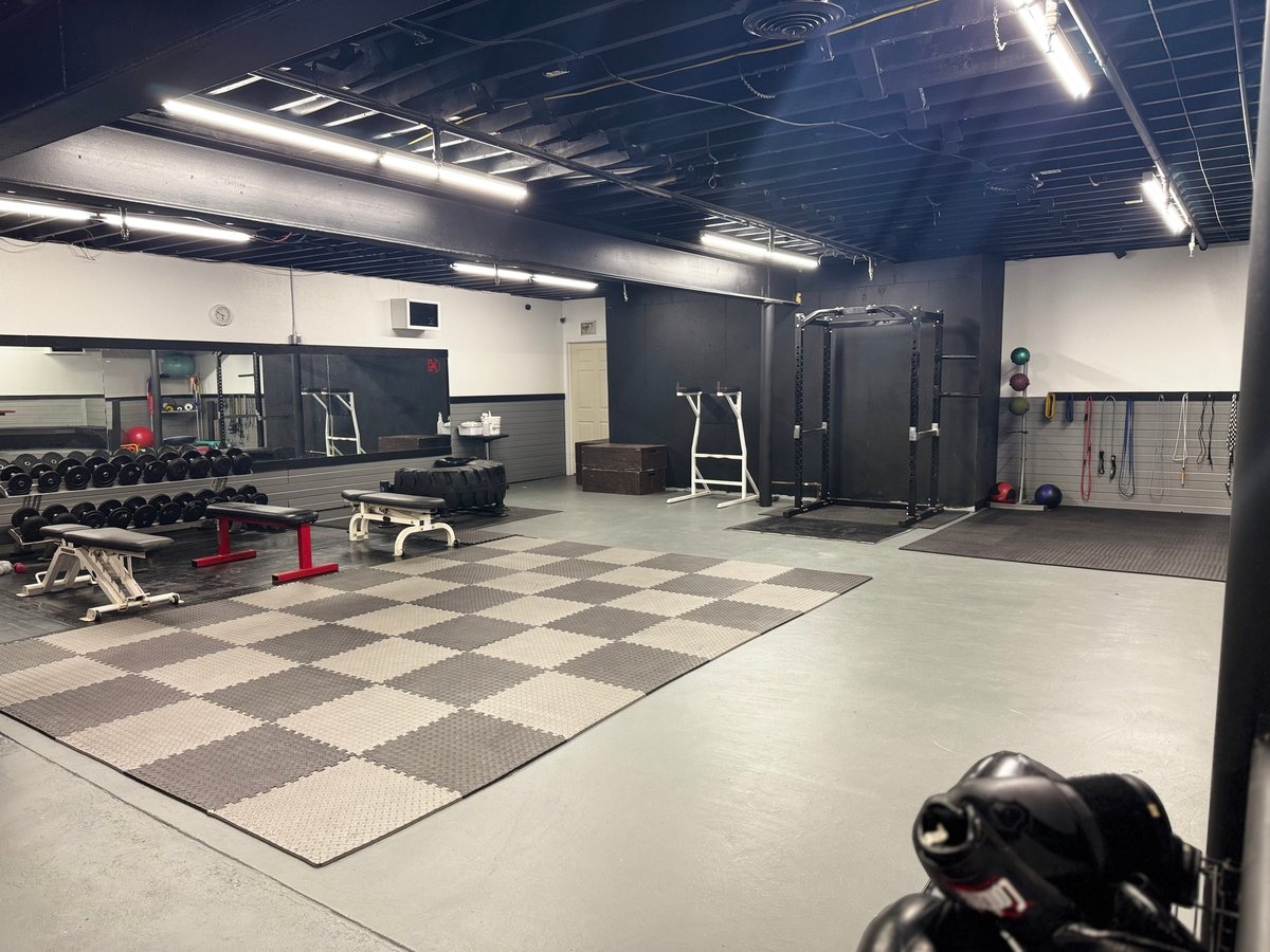 Modern gymnasium interior with checkered floor, exercise equipment, dumbbells, and mirrored walls under bright fluorescent lighting